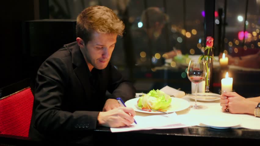 Blond man write and read document at table near window in restaurant