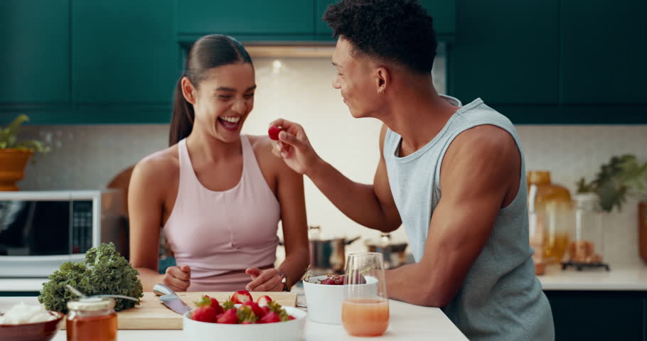 Fruit, health and eating with couple in kitchen for nutrition, bonding and fitness diet. Detox, cooking and recipe with man and woman with strawberry at home for morning, weight loss and fiber