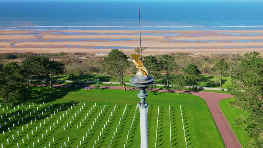 Golden eagle flagpole, Normandy American Cemetery with Omaha Beach in background, Colleville-sur-mer, France. Aerial drone orbiting