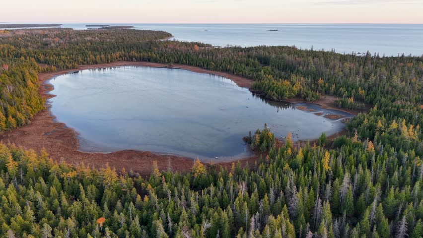 Aerial drone shot of a calm forest lake with colorful autumn trees in Michigan’s Upper Peninsula