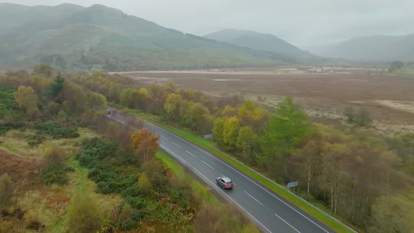 Stunning road through Scottish Highlands valley, misty cloudy aerial shot