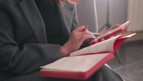Businesswoman writing in red notebook, holding pen, modern office environment, gray suit, focused on task, productivity, planning, decision-making, workspace, corporate setting, concentration - Powered by Shutterstock - Get 15% off with code: PIKWIZARD15