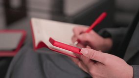 Close-up of person holding red phone in one hand and writing with red pen on notebook, showcasing focus on task at hand. Ideal for business meetings, office work, and productive sessions - Powered by Shutterstock - Get 15% off with code: PIKWIZARD15