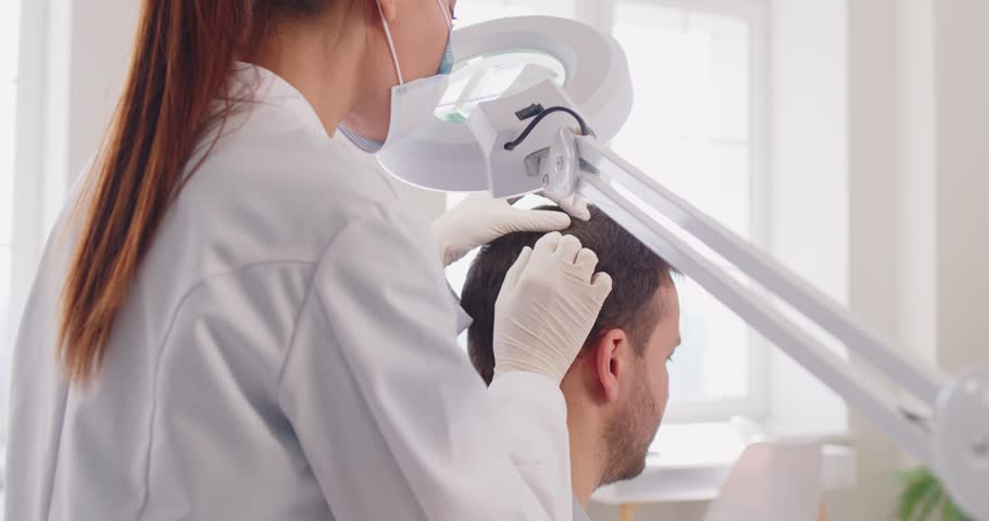 Trichologist doctor or nurse examines a patient hair and head in a clinic. Treatment for alopecia, dermatology, and scalp health, highlighting professional care in a medical environment.