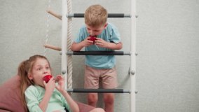 Happy siblings enjoying fresh fruit indoors, girl relaxing on pink bean bag chair eating apple while boy hangs on indoor ladder eating apple, cozy playful environment with soft pastel tones - Powered by Shutterstock - Get 15% off with code: PIKWIZARD15