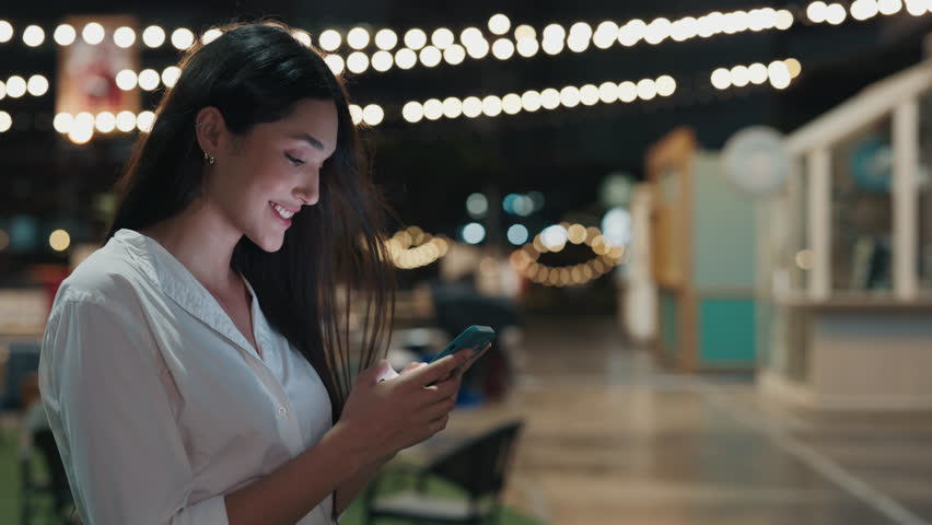 Owner Of A Night Cafe, Young Woman, Standing near Restaurant And Chats On Smartphone Outside. Young Boss Typing Text Message And Smiling While Looking At Phone. People and Technology Concept - Powered by Shutterstock - Get 15% off with code: PIKWIZARD15