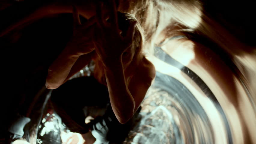 Female dancer making dramatic hand movements while seated among distorted reflections illuminated by swirling lights. Overhead view