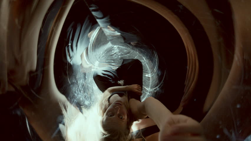 Female dancer performing dramatically in surreal mirrored space surrounded by swirling distorted reflections and flickering light. Directly above view