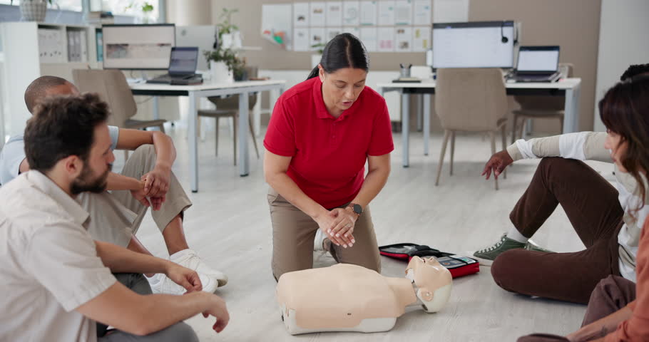 Office, first aid practice and training with people, explain and learning to use equipment on dummy. Workplace, floor workshop and instructor speaking to group, medical support and paramedic coaching