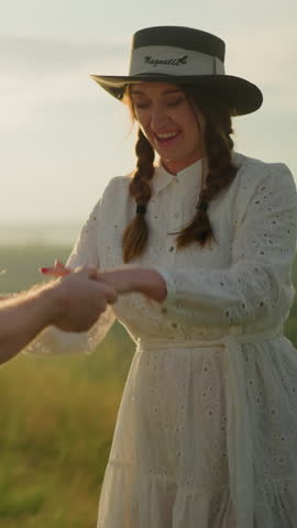 A close-up shot of two lovers dancing gracefully in a sunlit field, both dressed in white and wearing hats. The warm golden light enhances the romantic atmosphere as they share an intimate moment