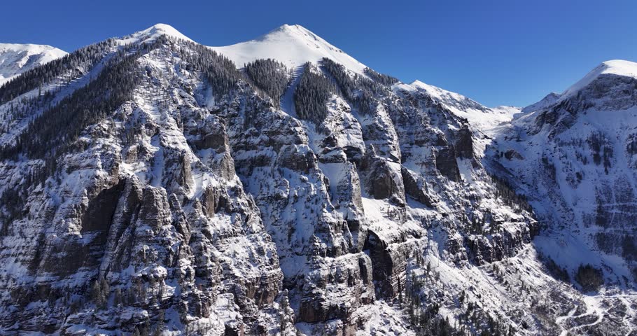 An unworldly aerial drone shot of the extreme Kroger Via Ferrata cliff face and the Black Bear pass switchbacks and summit, slowly tracking forward over the Telluride Valley floor in Western Colorado.