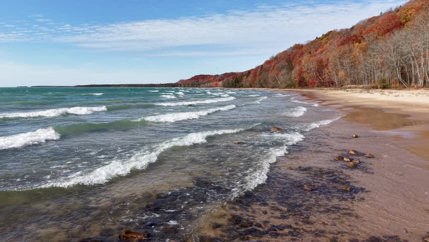 Aerial drone view of strong lake waves hitting a forested autumn shoreline along Michigan’s Upper Peninsula