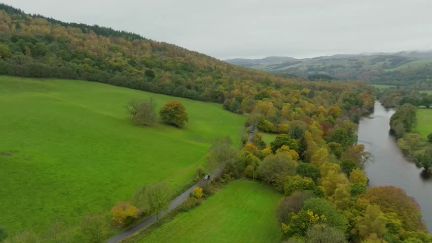 Car driving along stunning countryside road through Scottish Highland valley with rolling hills, aerial shot over scenic route