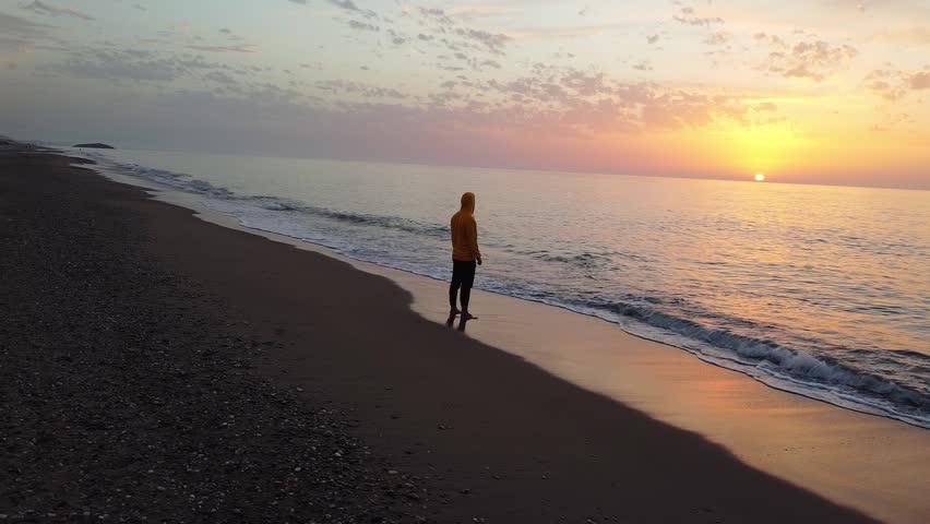 Lonely man relaxing on the beautiful beach at sunset. Sun reflected on beach, Lonely man stands on the beach looks towards the sun light. A man meets the sunset on beach, silhouette of person walking.