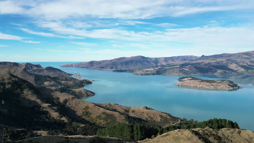 Scenic drone footage of the Port Hills near Christchurch, New Zealand, showing rugged hills, lush greenery, and clear skies on a calm day.