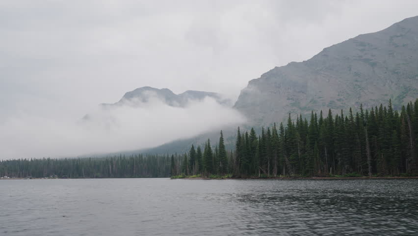 Misty mountain lake view with pine forest, clouds, and moody weather in Montana, USA
