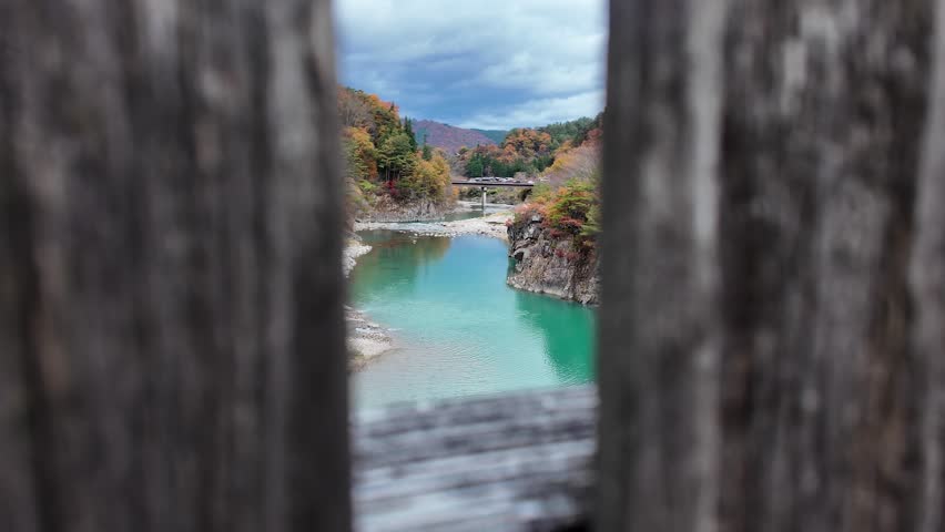 Sho River flowing amid vibrant autumn scenery, framed by wooden structure within Shirakawago.