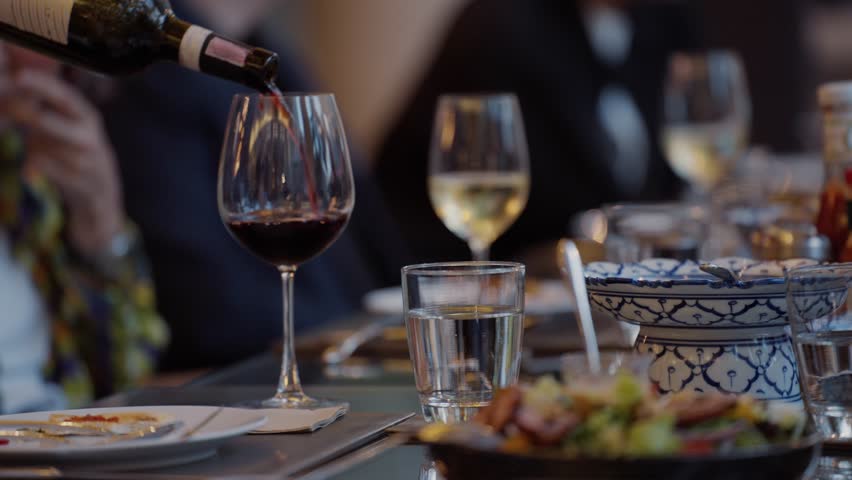 A waiter is pouring red wine into a glass on a dining table at a banquet event, Waiter pouring wine for customer at hotel restaurant. Exclusive dining event, sophisticated and celebratory