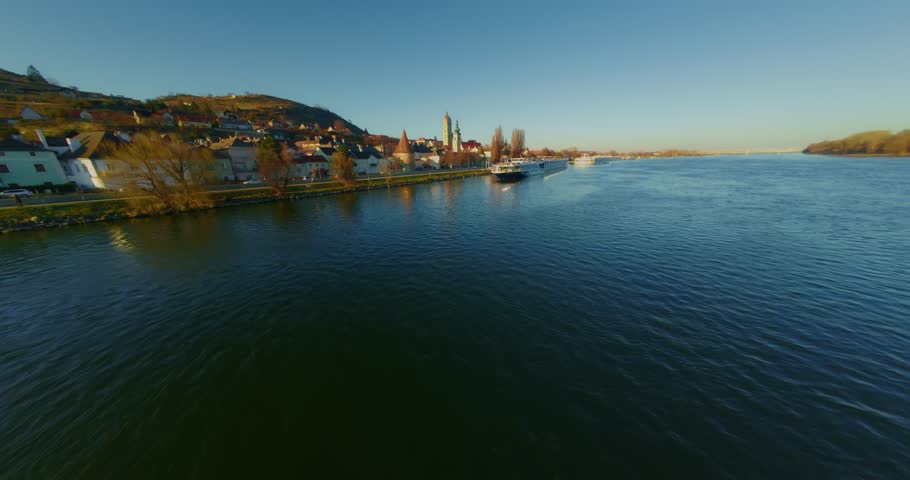 Aerial view of a cruise ship docking in Stein an der Donau, a charming town in Lower Austria, during a beautiful sunset, showcasing the Danube River and the picturesque landscape, ramp fpv pov shot