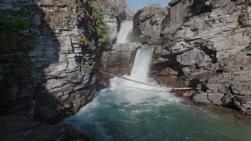 Waterfall crashing between rocky cliffs at St. Mary Falls, Montana, bright summer day