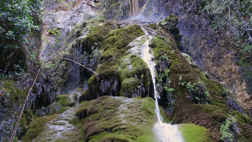 A stream of water falls gently onto a mossy rock surrounded by vibrant greenery at Kremioti Waterfall in Kritou Terra Cyprus