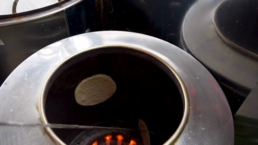 Traditional naan is baked on the inner wall of a tandoor oven over open flames in a Pakistani kitchen