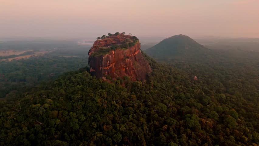 A breathtaking aerial view of Sigiriya Rock at dawn, with the ancient fortress illuminated by the soft first light of the day.