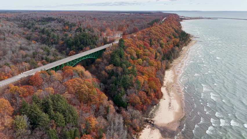 Drone footage of a bridge stretching along the Lake Michigan shoreline, framed by vibrant fall foliage in the Upper Peninsula