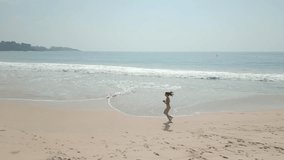 A young woman runs along a beautiful tropical beach in slow motion, viewed from above. This high-quality aerial concept is perfect for lifestyle, fitness, or travel promotions. - Powered by Shutterstock - Get 15% off with code: PIKWIZARD15