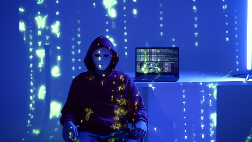 A mysterious hacker in an orange hoodie and white mask sits in a violet neon room with code projected around. A terminal-filled laptop glows in the back, visualizing secrecy and cyber tech