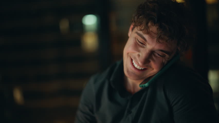 Portrait night manager calling cellphone discussing project. Smiling businessman talking mobile phone at dark corporate workplace. Cheerful entrepreneur holding pencil enjoy smartphone conversation.