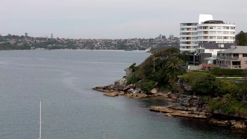 A coastal vista,in Manly, Sydney, featuring rocky cliffs, waterfront buildings, and a view across the harbor towards the city skyline
