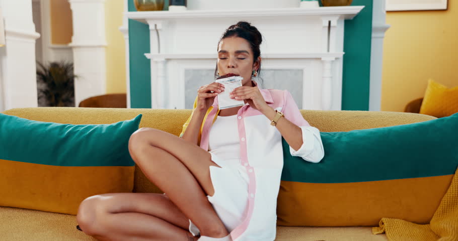 Tv, eating and woman with chocolate to relax or taste snack with cocoa flavor and smile in home. Apartment, television or girl with sweet treat and sugar craving with remote control or cheat meal