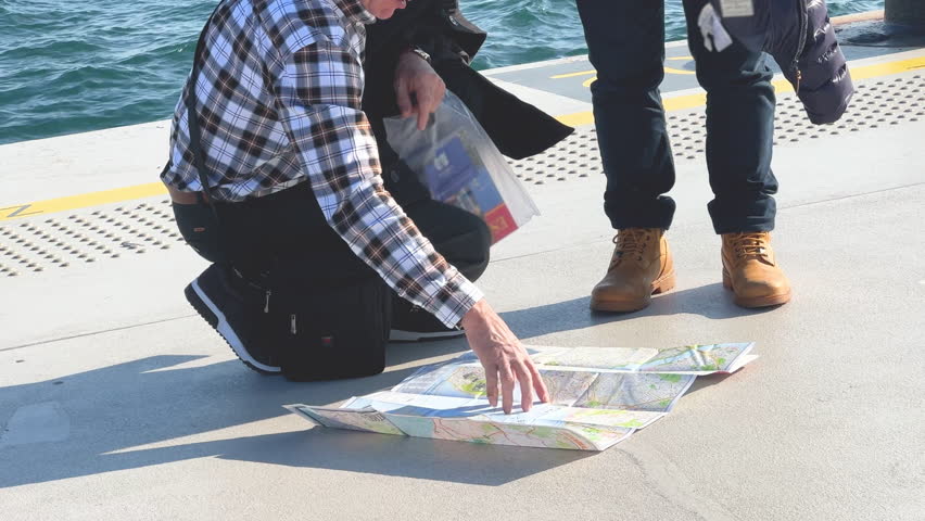 Two old mature travelers study map on sunny pier. Tourist man points to location, trip discussion. Adventure and exploration. Curiosity and spirit of travel. Tourism, explore new city, country.