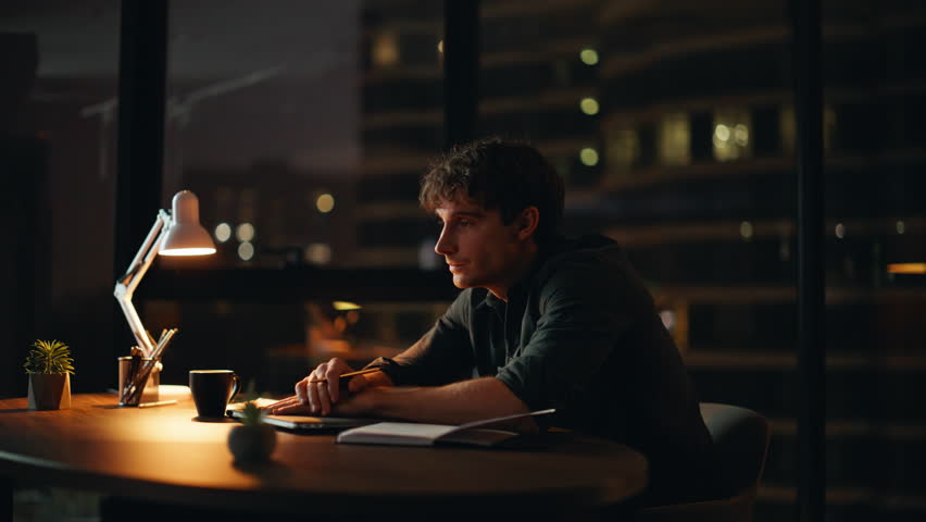 Fatigued employee sitting dark workplace with closed laptop. Overworked businessman rubbing eyes drinking coffee at night office. Overloaded man manager feeling burnout after late overtime work indoor