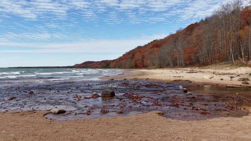 Aerial footage of a rugged beach shoreline with autumn forest bluffs along Lake Superior in Michigan’s Upper Peninsula