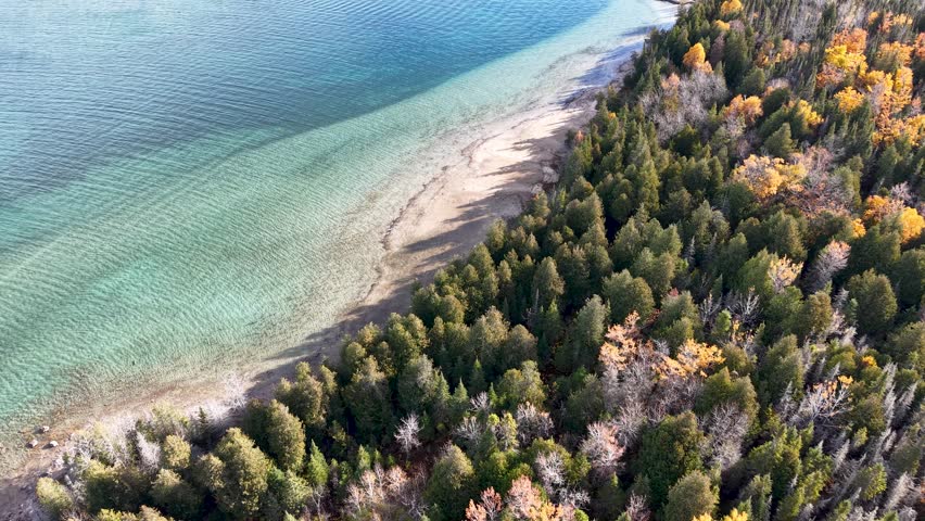 Drone view of a secluded Lake Huron shoreline lined with evergreen and deciduous forest in Michigan’s Upper Peninsula