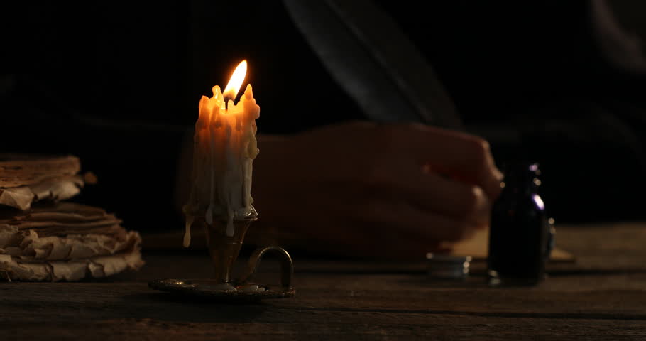 Woman writing with fountain pen at wooden table in darkness, focus on burning candle in candlestick