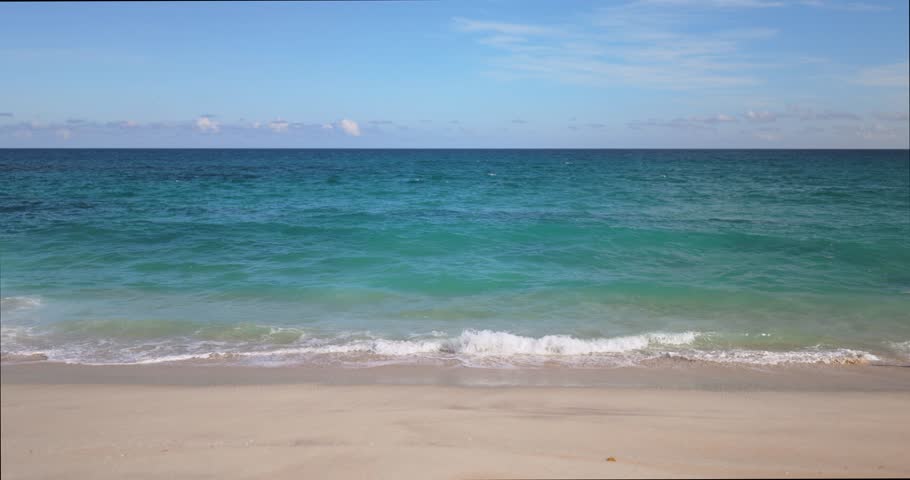 A tranquil view of a man in a hat standing and walking along a sandy beach with turquoise ocean waves. Ideal for themes of leisure, travel, and serene moments. 