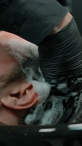 Close-up of bearded man head washed with shampoo foam in a barbershop with gloves. Professional and proper hair care. Cutting hair and beard. Vertical shot.