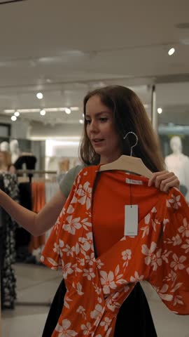 The girl in the store asks the guy's advice choosing between two dresses. The couple in love came to the store of modern clothing for shopping. Shopping on the weekend concept Vertical shot.