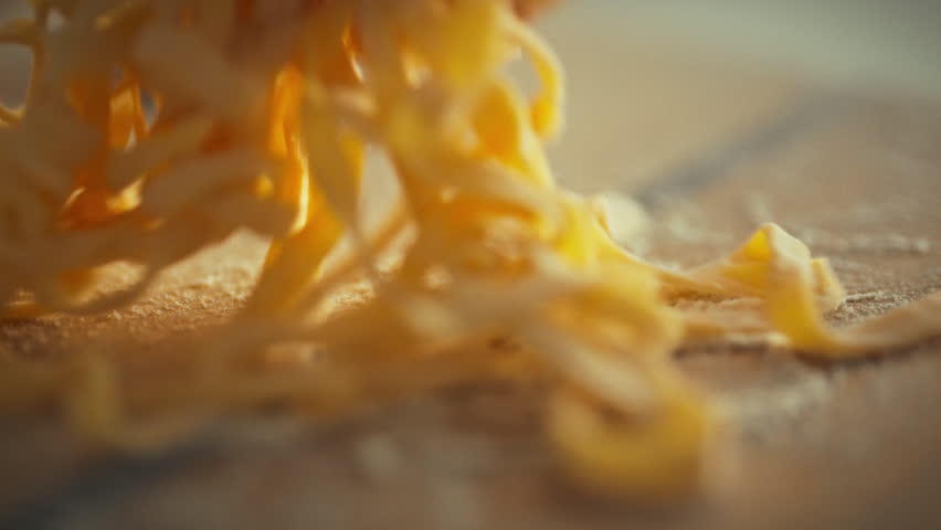 A hand gently places freshly made pasta on a wooden surface, showcasing the delicate texture and care involved in preparing traditional Italian cuisine. It reflects the artistry of cooking