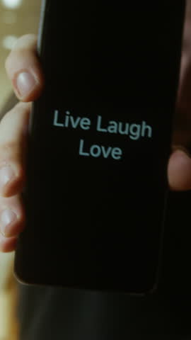 Cheerful Young Man Holding Smartphone Displaying Live Laugh Love Message in Bright Kitchen Environment ,vertical video