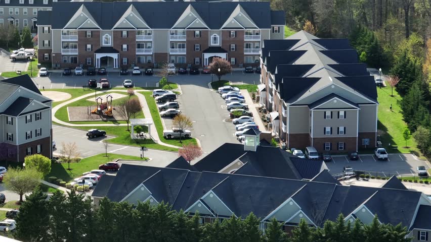 Typical American residential complex architecture with townhouses or apartments.Suburban style includes gabled roofs, porches and brick siding with communal playground. Aerial view. Spring day in USA.