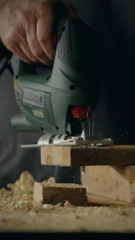 In a well-equipped workshop, a master wood carpenter carefully operates an electric jigsaw to cut a piece of wood. This action demonstrates precision woodworking craftsmanship in progress