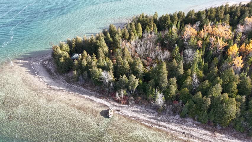 Aerial view of a rocky shoreline in Michigan’s Upper Peninsula, surrounded by vibrant forest and turquoise freshwater