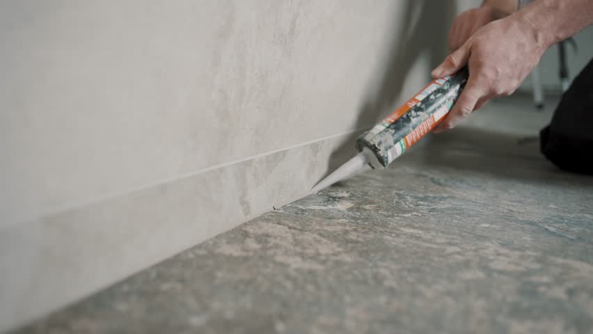 Slow motion tile installation by man sealing edges with caulk in a modern home setting