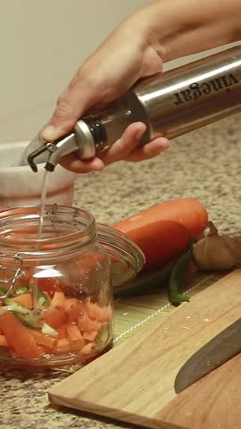 Pouring vinegar to a jar of carrots and green chili before shaking it, quick and simple homemade pickle recipe for a healthy and sustainable home life
