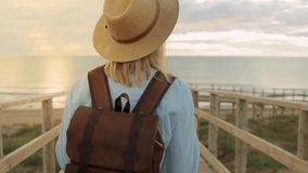Woman hiking wooden boardwalk at sunrise, wearing straw hat and backpack, basking in golden morning light during coastal wandering.Europe travel. Lifestyle, vacation, tourism, nature, active life - Powered by Shutterstock - Get 15% off with code: PIKWIZARD15