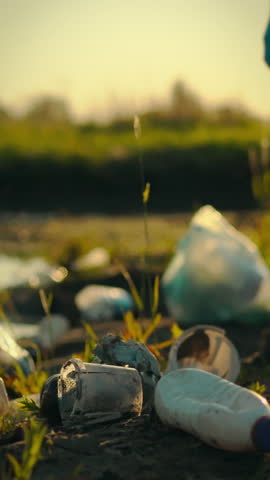 A caring young man wearing gloves collects and sorts plastic garbage into bags during a community cleanup event in a rural setting. The sun sets, highlighting his efforts to protect the environment